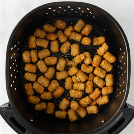a black air fryer filled with tater tots.