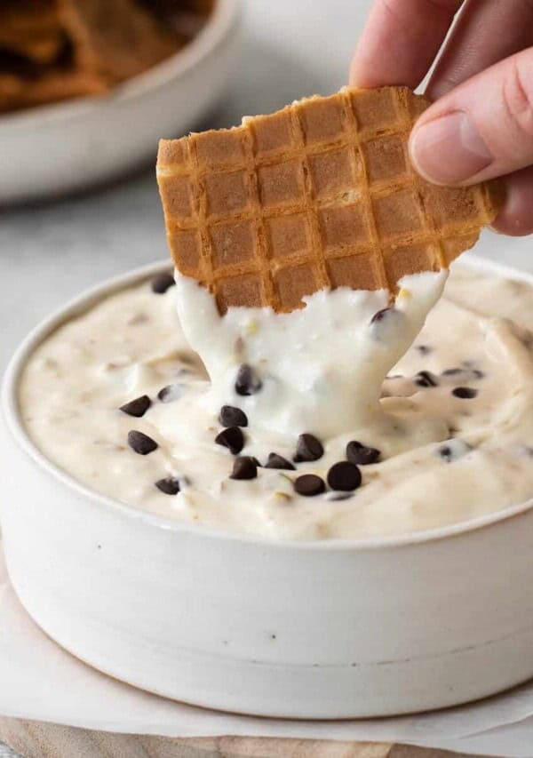 Waffle cone being dipped into cannoli dip.