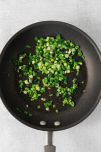 fried green onions in a frying pan on a white background.