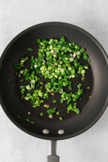 fried green onions in a frying pan on a white background.