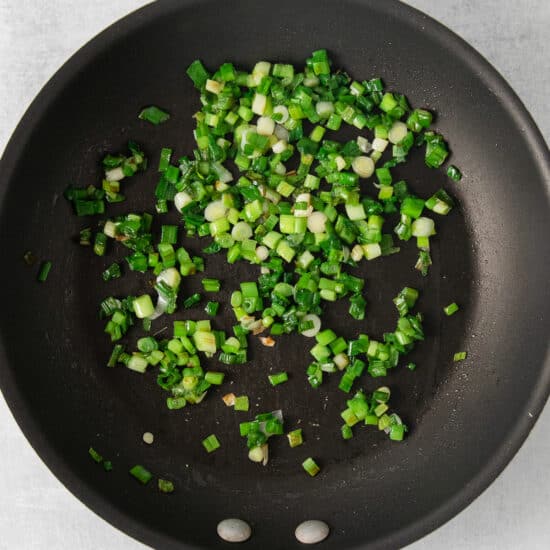 fried green onions in a frying pan on a white background.