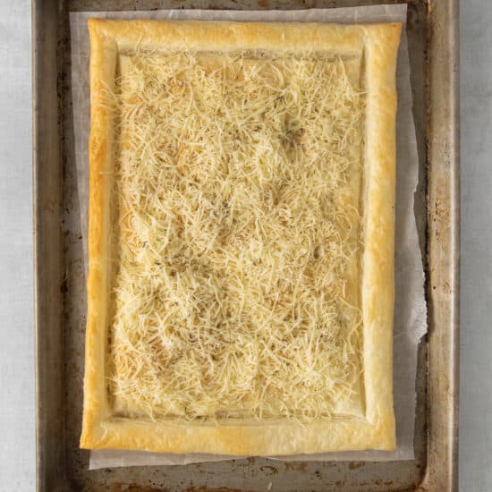 a square pastry with cheese on a baking sheet.