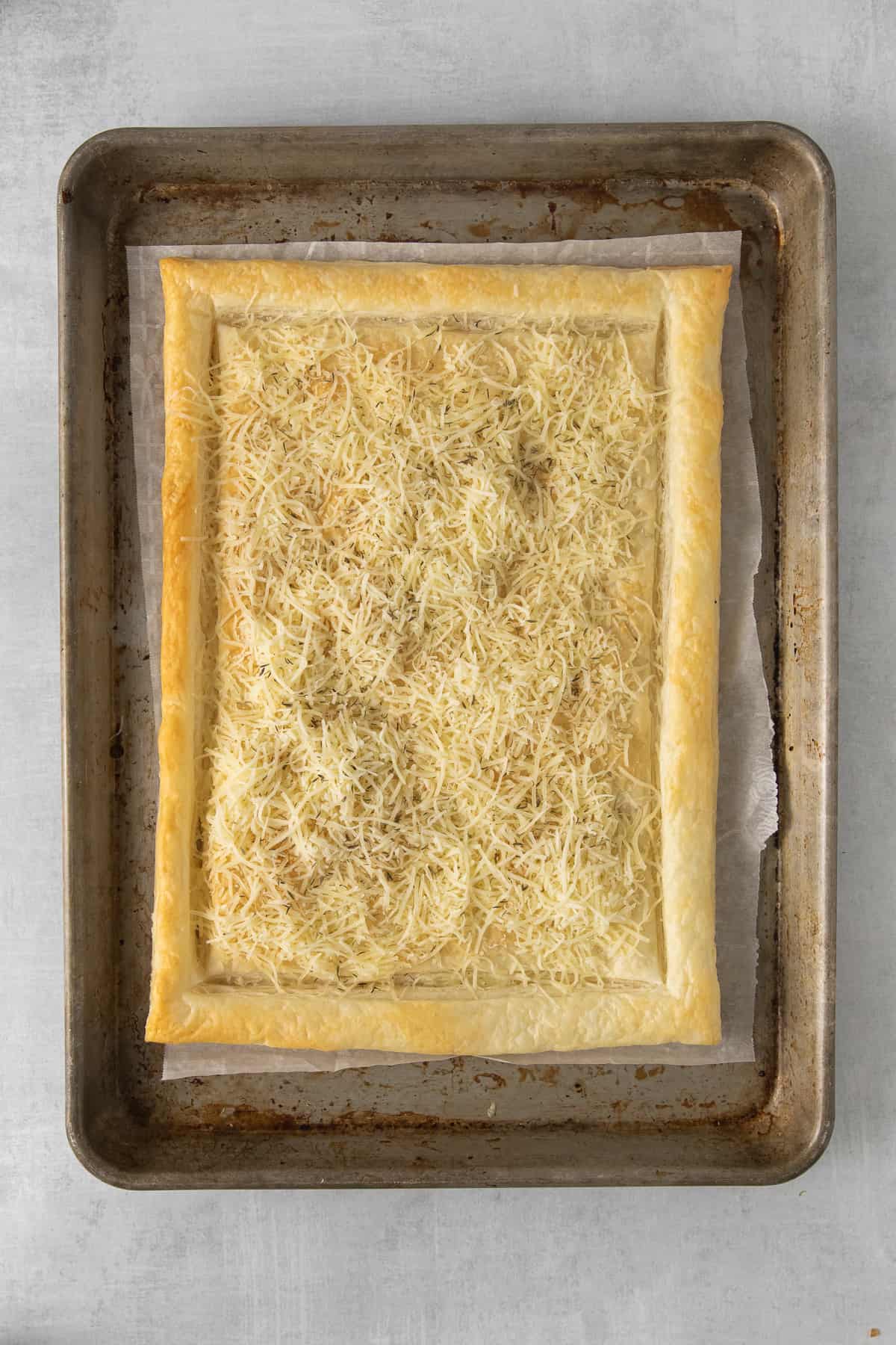 Puff pastry topped with shredded gruyere on a baking sheet.