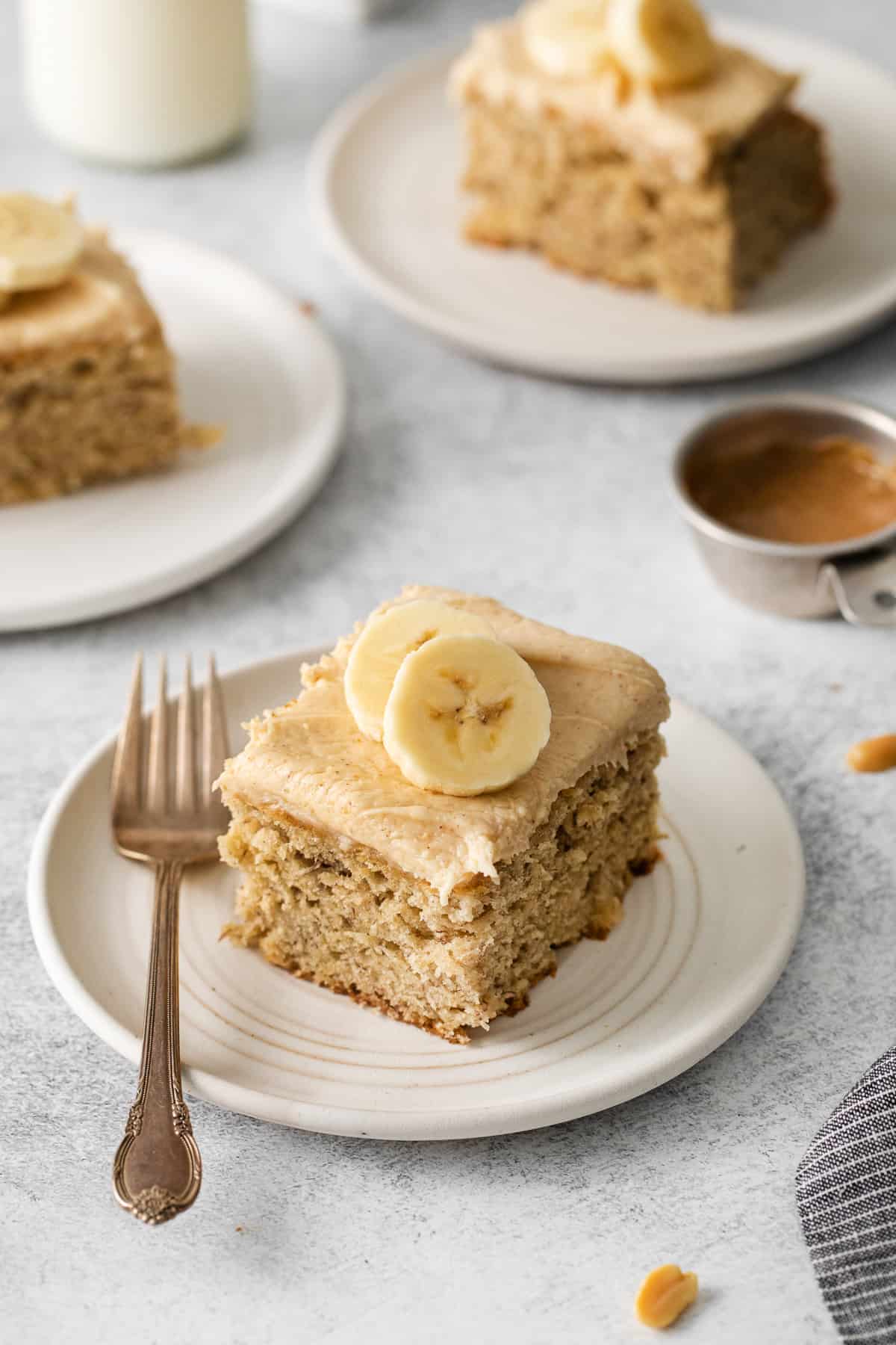 Slice of banana cake with cream cheese frosting on a plate.