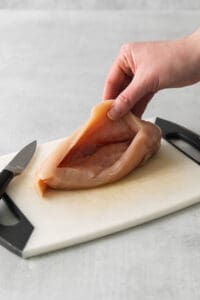 a person cutting a piece of chicken on a cutting board.