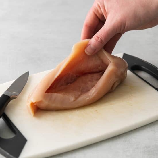 a person cutting a piece of chicken on a cutting board.