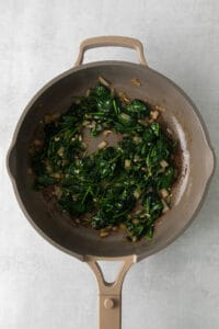 a frying pan filled with spinach and onions.