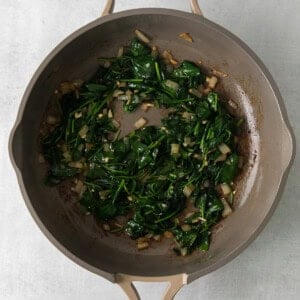 a frying pan filled with spinach and onions.