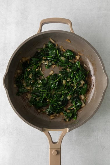 a frying pan filled with spinach and onions.