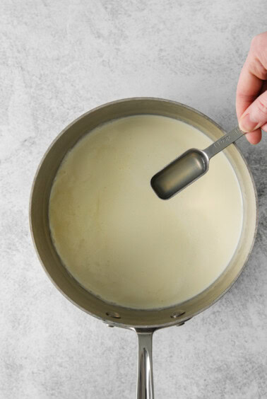 a person pouring milk into a pan.