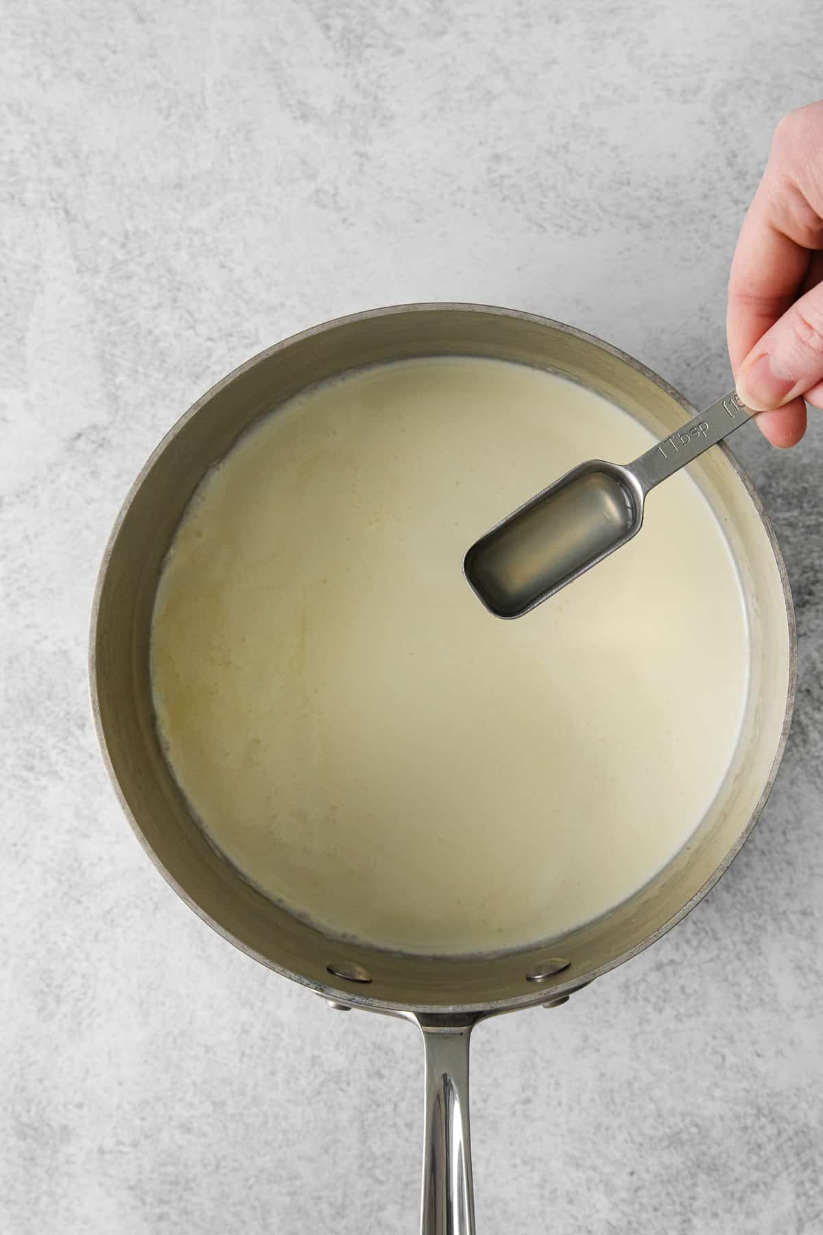 Lemon juice being poured into heavy cream in a saucepan.