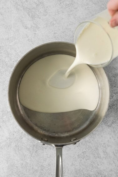 a person pouring milk into a pan.