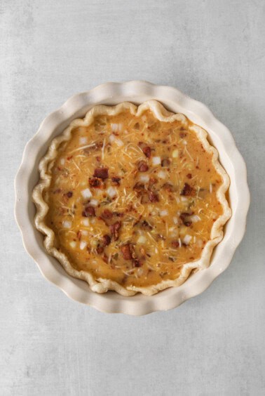 a pie with cheese and bacon in a white dish.