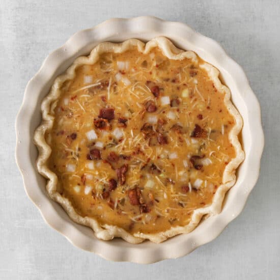a pie with cheese and bacon in a white dish.