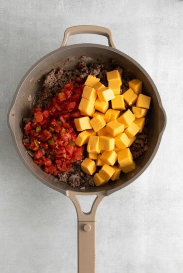 a frying pan filled with meat, cheese and tomatoes.