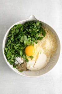 a white bowl filled with eggs, cheese, parmesan, and parsley.