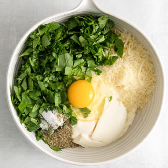 a white bowl filled with eggs, cheese, parmesan, and parsley.