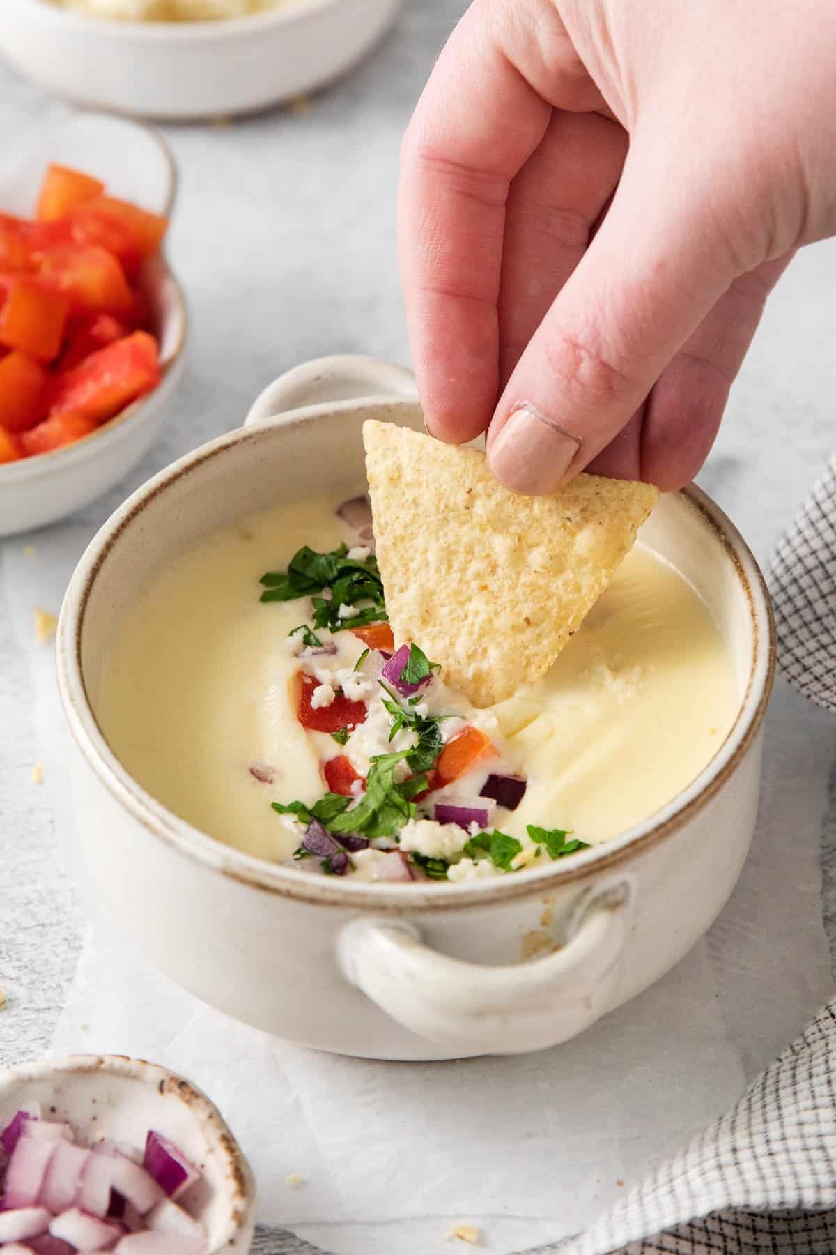 A tortilla chip being dipped into cotija queso dip.