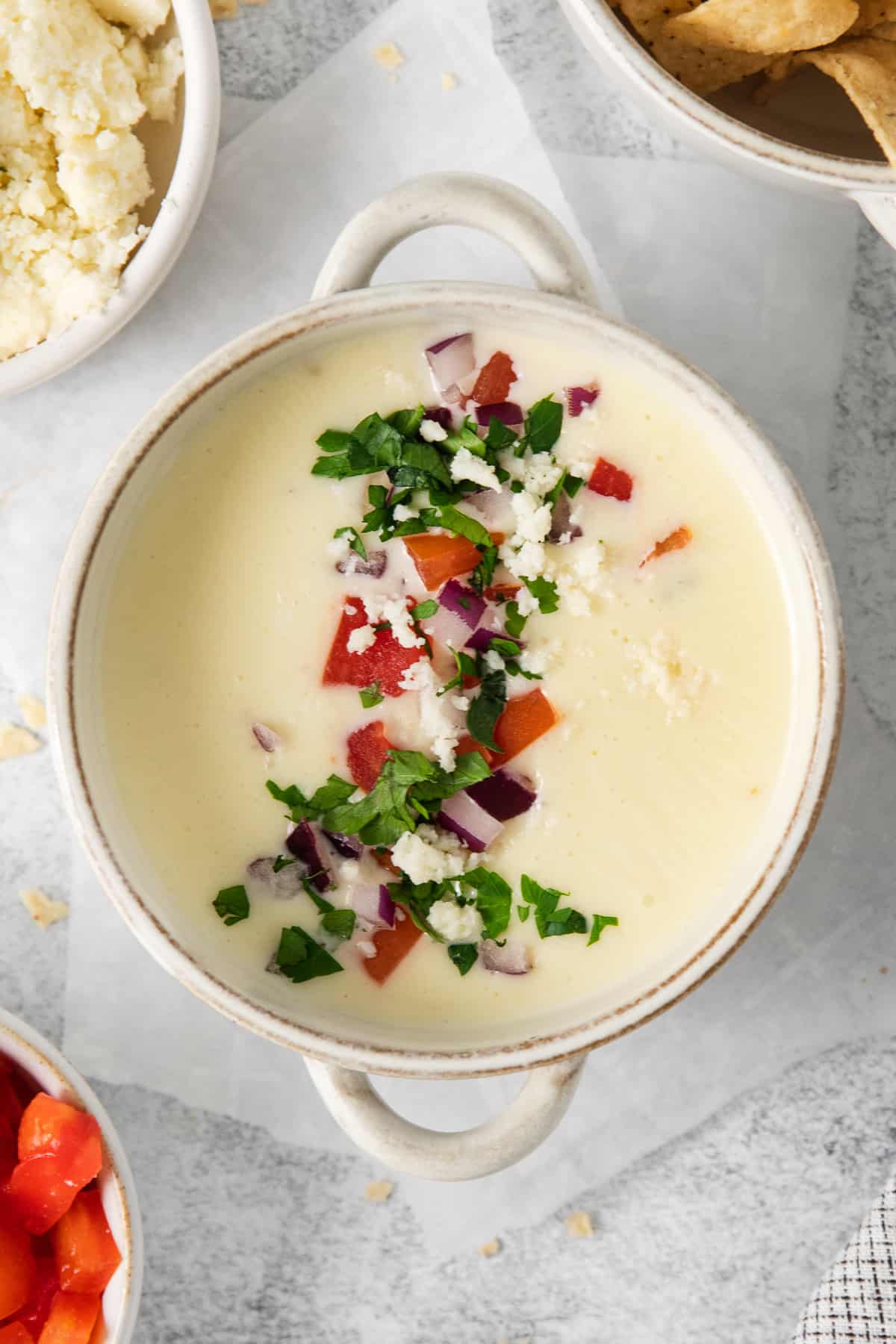 Cotija queso dip in a bowl topped with tomatoes, onion and cilantro.