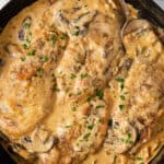 Chicken breasts in creamy mushroom sauce cooked in a skillet.