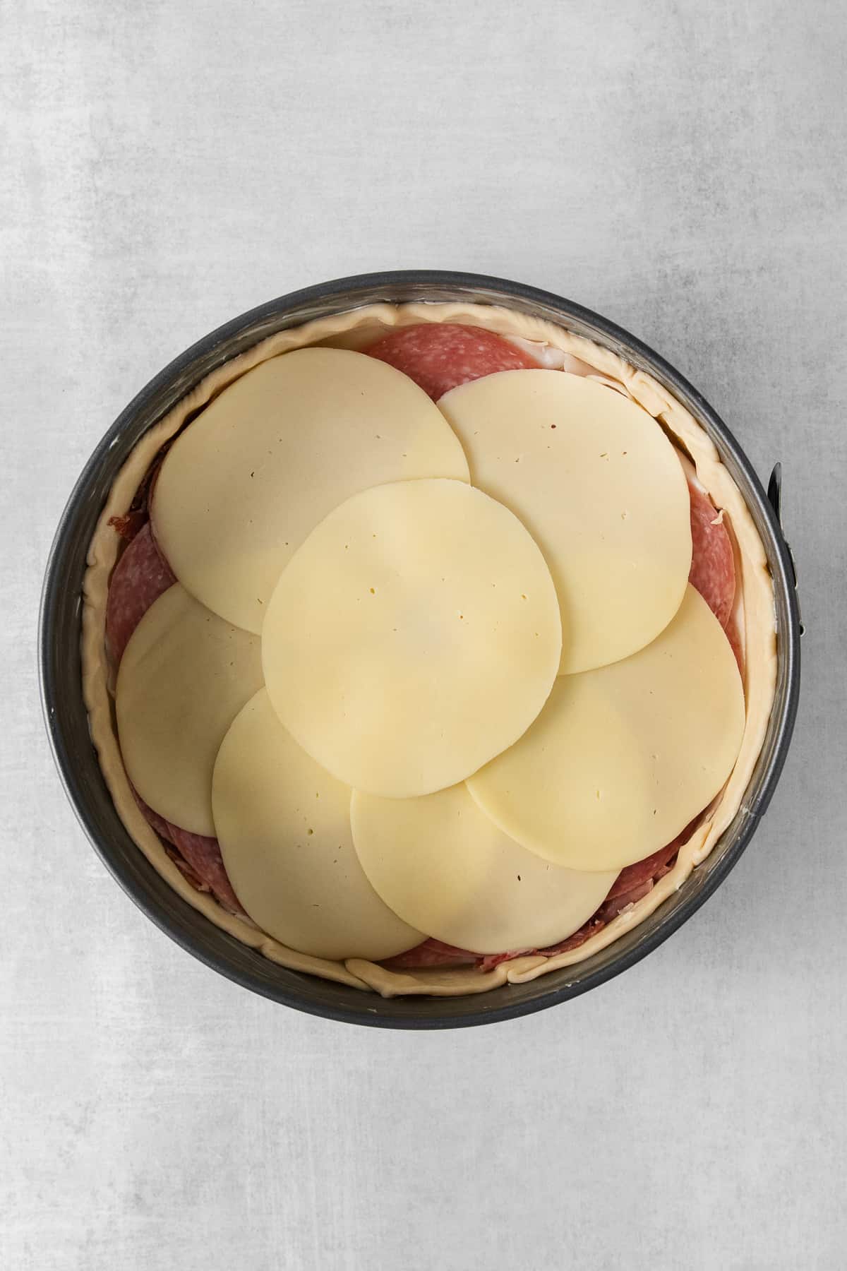 Salami and sliced provolone in a spring form pan.