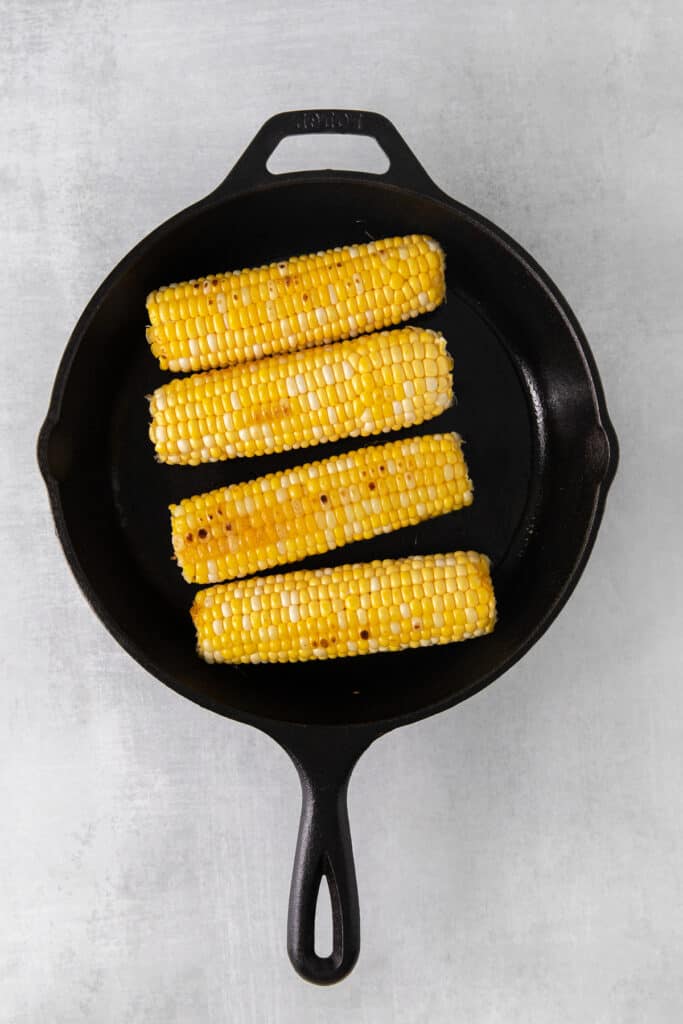 Corn on the cob browning in a cast iron skillet.