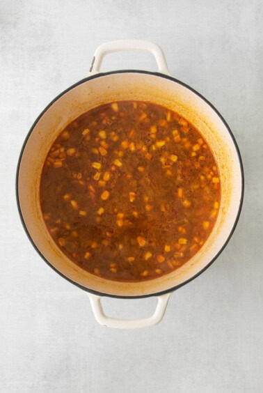 a pot of soup with beans and corn on a white background.