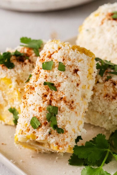 corn on the cob with cilantro and lime on a white plate.