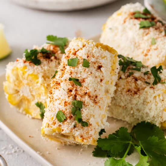 corn on the cob with cilantro and lime on a white plate.