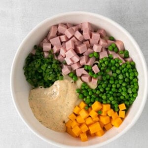 ham, peas, carrots and dressing in a white bowl.