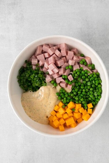 ham, peas, carrots and dressing in a white bowl.