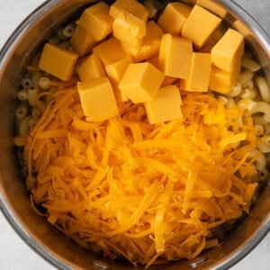 Shredded and cubed cheese in a pot with macaroni noodles.