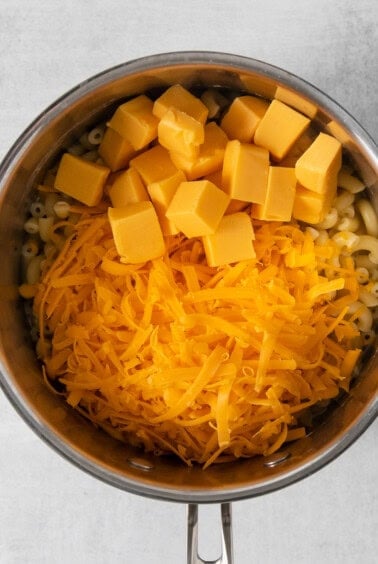 Shredded and cubed cheese in a pot with macaroni noodles.