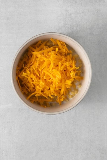 shredded cheese in a bowl on a gray background.