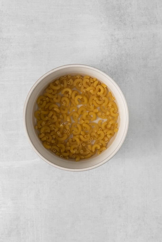 Macaroni noodles in a bowl of water.