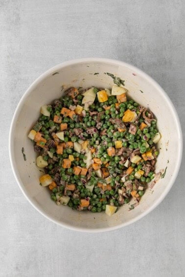 a white bowl filled with peas, carrots and meat.