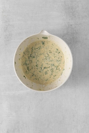 a white bowl with a green sauce on it.