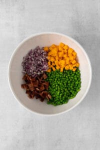 peas, carrots, onions and bacon in a white bowl.