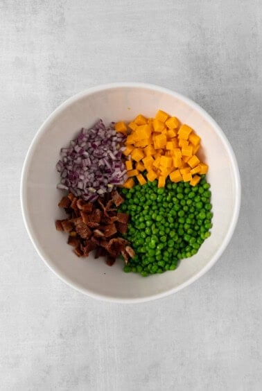 peas, carrots, onions and bacon in a white bowl.