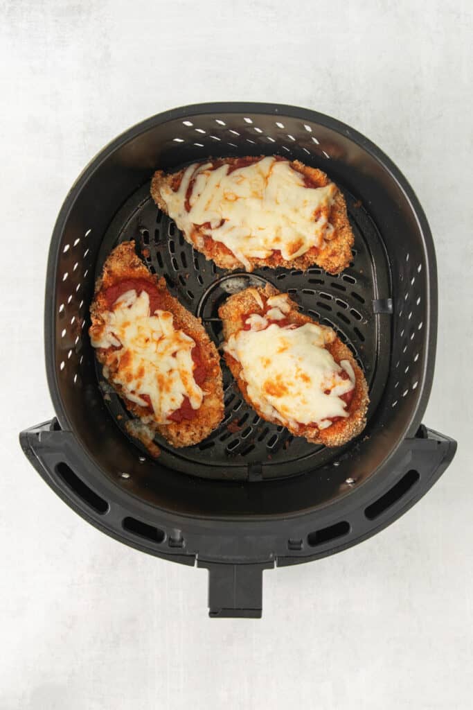 a black air fryer with pizza in it.