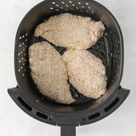 a black air fryer with chicken in it.