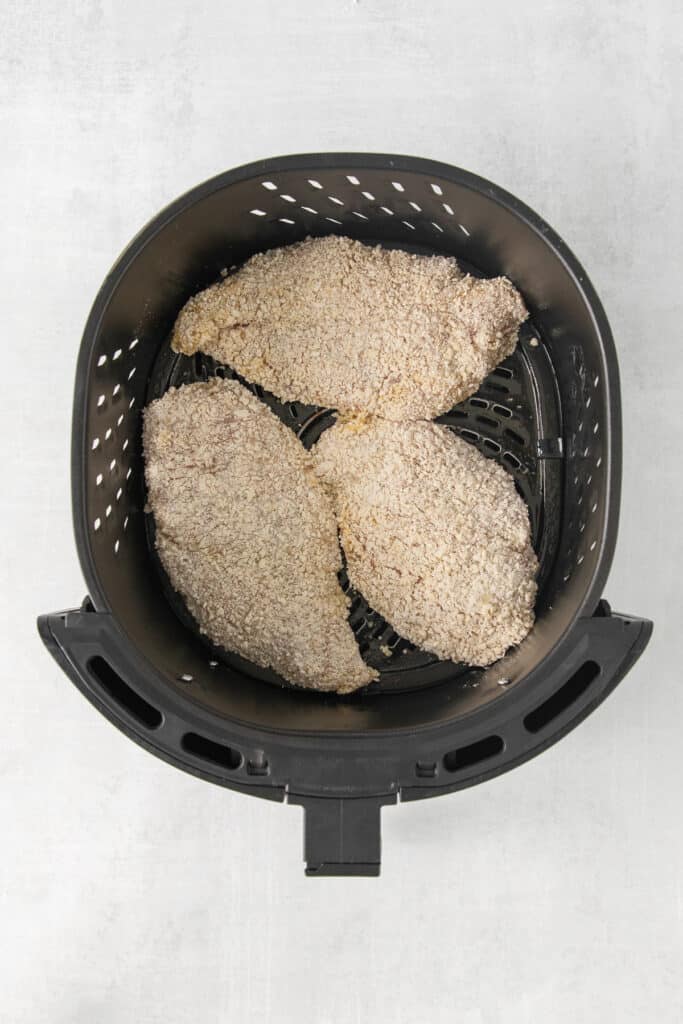 a black air fryer with chicken in it.