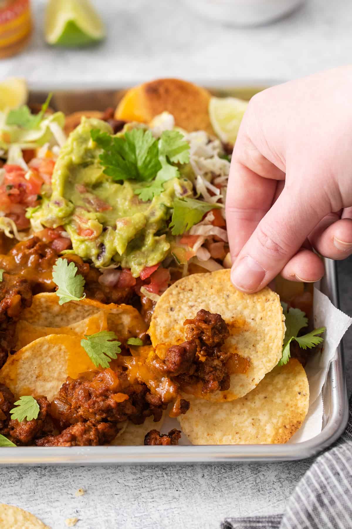 A hand grabbing a tortilla chip with ground beef on it.