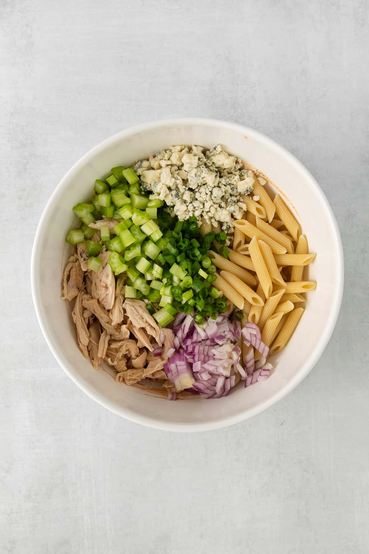 Ingredients for buffalo chicken pasta salad in a bowl.