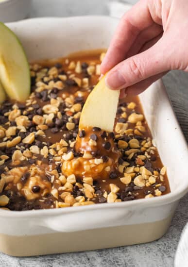 a person dipping an apple into a baking dish.