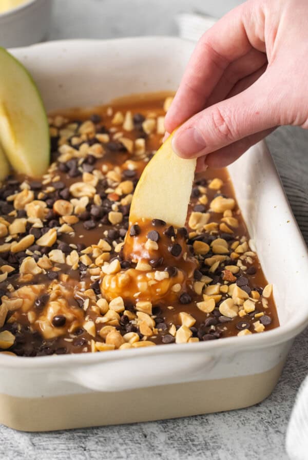 a person dipping an apple into a baking dish.