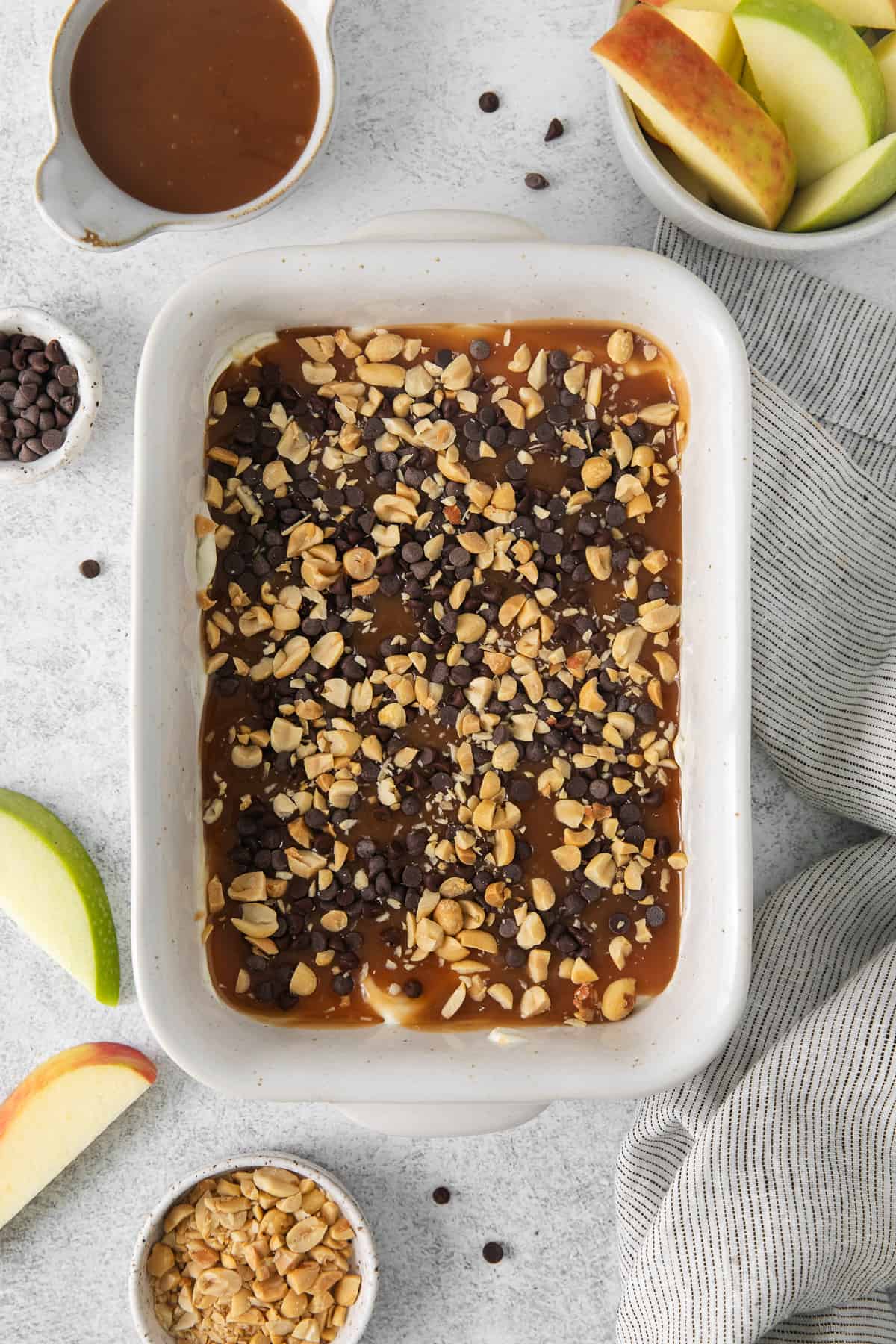 a white dish with apples, nuts, and granola.