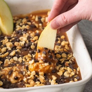 a person dipping an apple into a baking dish.