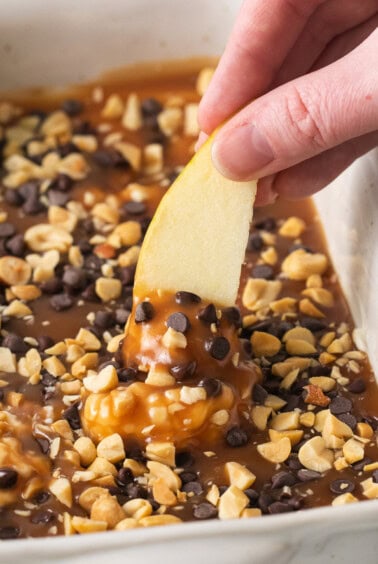 a person dipping an apple into a baking dish.