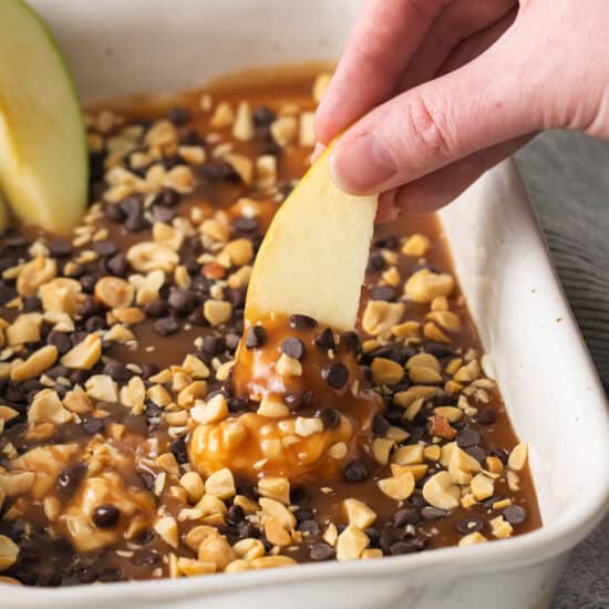 a person dipping an apple into a baking dish.